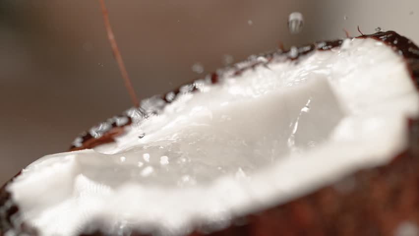 MACRO, DOF, SLOW MOTION: Cinematic shot of water droplets splashing into the ripe tropical coconut. Refreshing coconut water overflows out of a brown hairy coconut shell with fragrant white flesh. | Shutterstock HD Video #1024777391