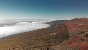 Aerial shot. Flying above the clouds against the backdrop of a highland forest of pine needles and a red volcanic landscape. Mountain range from a height. Canary Islands, Teide volcano. National park
