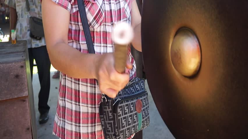 A woman bangs on a large Antique traditional Gong. 