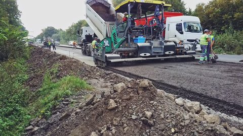 VINNITSA, UKRAINE - MAY 2018: A truck tosses over bitumen into a wide paver to lay a new roadway surrounded of repairmen. Road construction equipment. Aerial view.