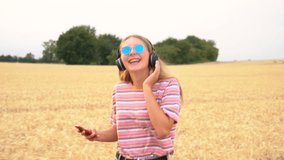 Slow motion tracking video clip of pretty blonde girl teenager young woman wearing a striped t shirt and blue sunglasses walking listening to music on her cell phone and wireless headphones 