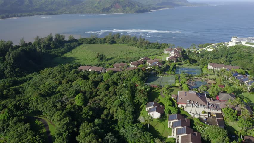 Hanalei Bay resort with tennis courts and pool in beautiful aerial 4k drone reveal view, Kauai North Shore, Hawaii. Shoreline, beach, palm trees and waves in tropical paradise  