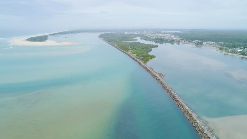Cinematic aerial pan descending and revealing beautiful coastline and breakwall at Harrington, NSW, Australia
