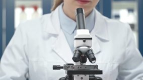 female scientist in white coat looking through microscope in laboratory