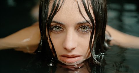 beautiful woman emerging her face from a bath looking at the camera in slow motion. girl taking a bath facing the camera