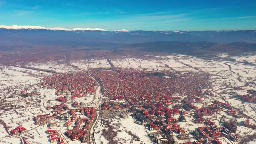 Panorama of the mountains and pine and spruce forests. Aerial view on the winter resort town of Bansko, Bulgaria, slide from the drone. Ethnic residential homes with snow-covered red roofs