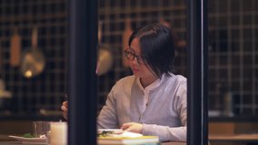 View Through window glass: Short-haired, glasses-wearing Chinese women are having dinner in restaurant, using phone while eating lunch,Businesswoman with mobile phone lifestyle 4k clip