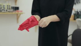 A female hairdresser putting on a red glove. Female hairdressed in black dress putting on red rubber glove. Salon safety tips.