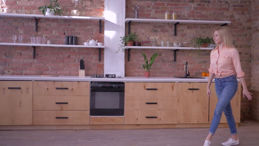 active cheerful girl doing gymnastic flip and sending air a kiss in slow motion at kitchen