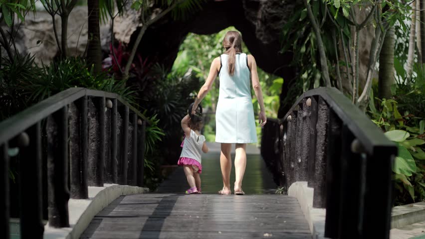 Asian mother and daughter walking together in the park on the bridge.