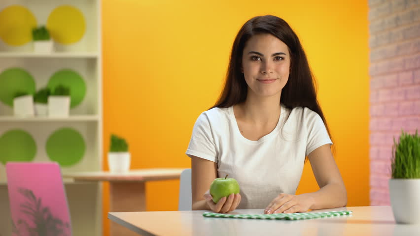 Smiling beautiful lady holding green apple hand sitting table, health care, diet