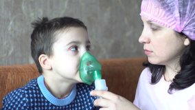 A young woman in a pink hat. A little boy makes inhalation. Room in the house. Human health. Nurse. 4K video