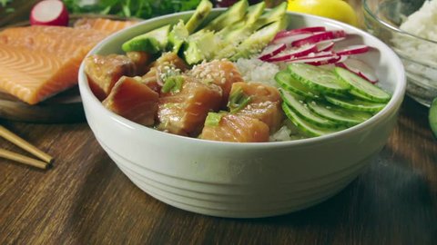 Poke bowl, traditional Hawaiian raw fish salad with rice, avocado, cucumber and radish on wooden background