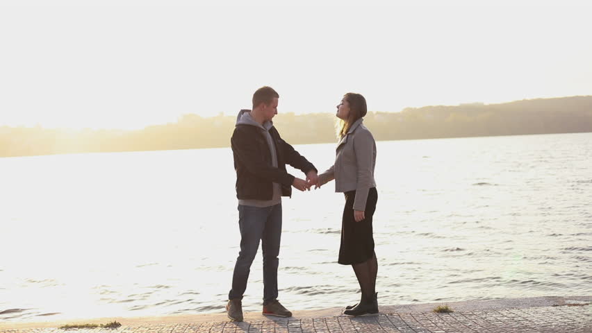 Happy young couple on the evening walk at city lake, plays with dog. Slowly