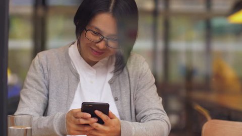 Close up of one Asian businesswoman using a mobile phone by the window in the cafe shop, typing on the smartphone, urban lifestyle with mobile phone 4k clip. Happy woman playing with smartphone.