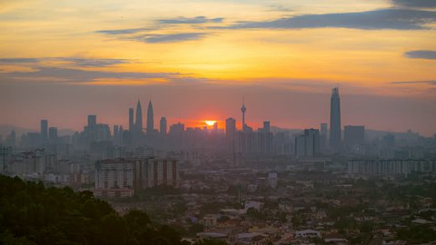 Timelapse of Kuala Lumpur city skyline cityscape starting at the sunset ending at night from afar with yolk sun in Federal Territory, Malaysia. Pan down motion timelapse.