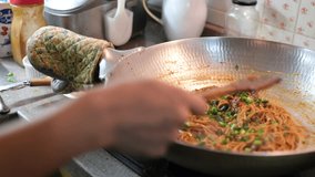 Frying noodles in a wok in the kitchen. Selective focus. Panning to the right.