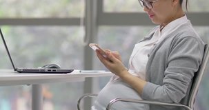Side view of one Chinese pregnant businesswoman working with laptop in the office, Asian adult woman typing on smartphone and communicating with the clients Asian working female in pregnancy 4k clip