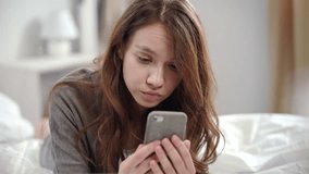 Shocked woman watching video news online on mobile phone at morning. Surprised woman face looking at smartphone in bedroom. Close up of young woman looking shocked video online on mobile phone