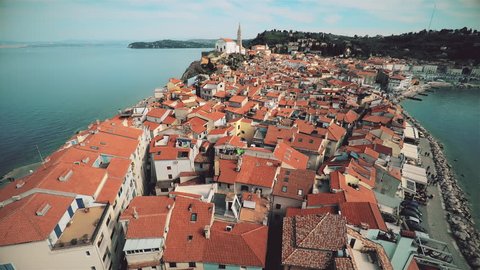 Aerial shot of Piran city surrounded by the sea. Flying over the roofs of Piran city on a sunny day.