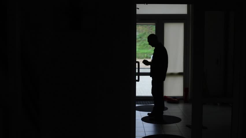 Silhouette of middle aged Caucasian male taling on phone with a door in the background.