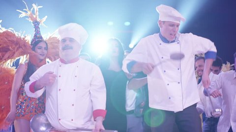 Cook and waiter dancers having fun dancing at a colorful party . Funny cook chef and waiters in white uniform, with a hat and ladle , smiling and partying during party . Cinema Camera in slow motion .