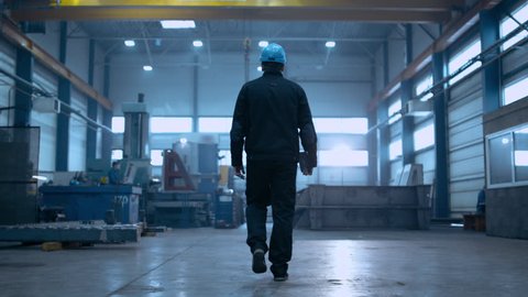 Following Shot of Professional Factory Worker Wearing Hard Hat Holds Tablet Computer, Walking Thorugh Modern Industrial Manufacturing Facility