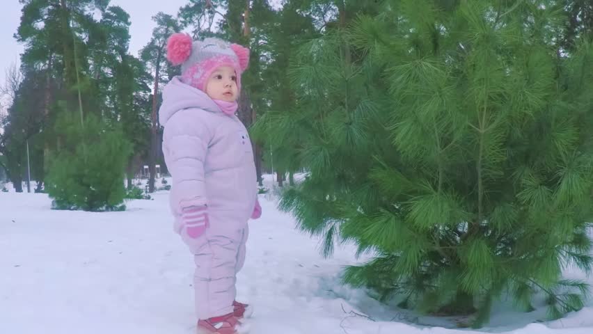 Little girl in the winter forest near the pine tree waving her hand
