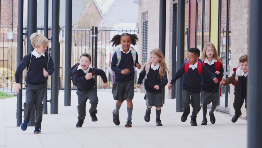 Happy primary school kids in uniforms running on a walkway outside their school building, front view Royalty-Free Stock Footage #1024874087
