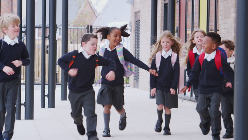 Happy primary school kids in uniforms running on a walkway outside their school building, front view | Shutterstock HD Video #1024874087