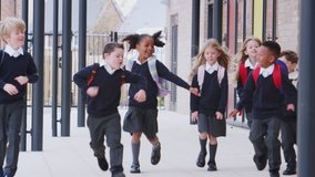 Happy primary school kids in uniforms running on a walkway outside their school building, front view - Powered by Shutterstock - Get 15% off with code: PIKWIZARD15