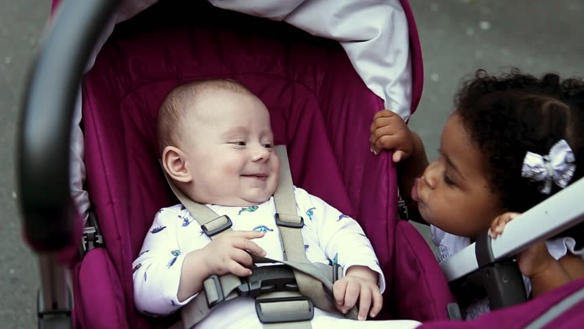 Two muliethnic children in the park. A little girl plays with a boy. Little Boy in the cradle