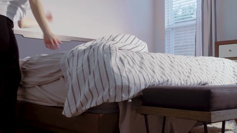 Slow motion low angle view of a person fixing the bed, lifting and airing the duvet, 23.98 fps.