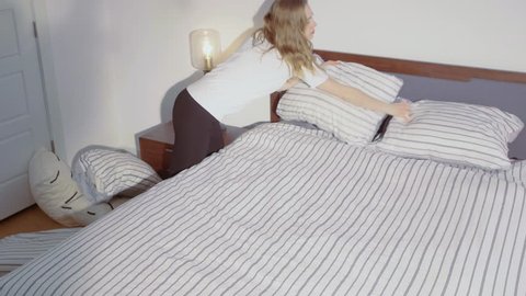 Top to bottom rotational camera angle of a girl fixing her bed, arranging her pillows and cushions neatly, 60 fps.