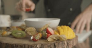 Man's hand puts half of strawberry on wooden plate. 4K slow motion video