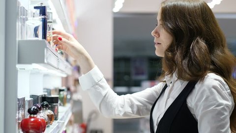 Brunette woman (model released) at airport perfumery shop, take one bottle from shelf, turn in hands and look beside. Close up shot of typical customer in duty free store at terminal sterile area