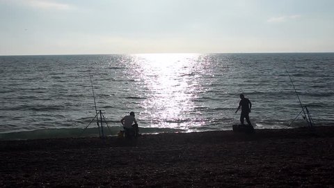 Two anglers silhouette at Seaford UK pebble beach
