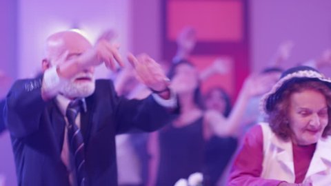 Stylish elderly couple having fun dancing at a colorful party . Sweet senior couple smiling and partying during party . Active retirement . Shot on RED HELIUM Cinema Camera in slow mo