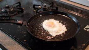 Frying chicken egg on a kitchen stove. Selective focus under low light. Tracking shot.