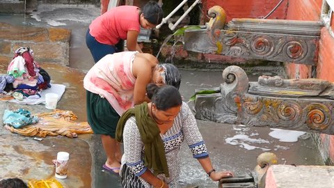 LALITPUR (PATAN), NEPAL - 12 OCTOBER 2018 People washing near temple wall. View of women washing hair and clothes with water from aged stone cranes in brick wall on street. Streetlife of Kathmandu.