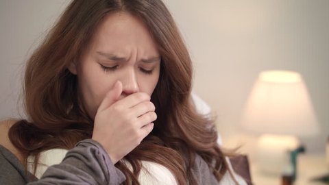Portrait of ill woman at home. Young woman coughing in bedroom. Close up of sick girl cough cold. Female person face with flu symptoms. Closeup of brunette woman squeezing