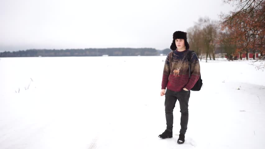 A handsome man hitchhiking. Young man hitchhiking on the road and smiling. A man travels to Siberia. Hitchhiking in winter. Beautiful Slavic male travelling alone. Young guy smiles and waves hand.
