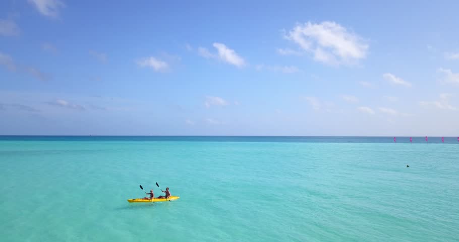 Man and woman paddle over serene empty ocean with perfect clear water on tropical island. 4k