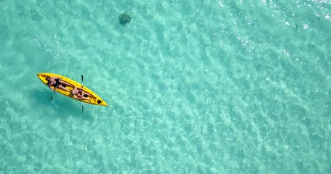 Looking down from above as two men paddle their yellow sea kayak through gorgeous clear blue water in Seychelles. Aerial, lookdown, 4k.