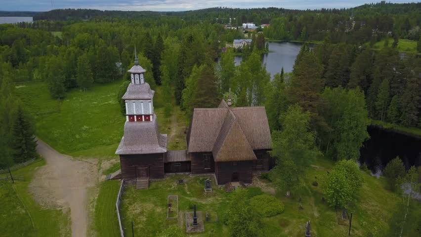 Aerial, tilt down, drone shot, above the famous, wooden church, in the middle of green trees, on a cloudy, summer day, in Petajavesi, Middle Finland