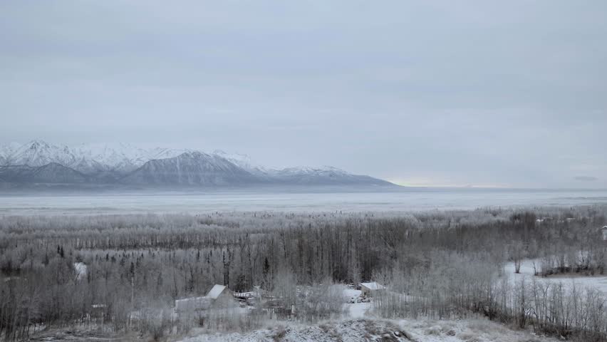 Alaskan frozen landscape, cabins hidden among trees and mountains in distance, Aerial pullback