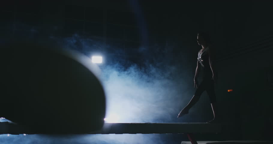 Women's Artistic Gymnastics. In slow motion in the smoke, the girl performs complex elements of the Olympic program on a balance beam. Royalty-Free Stock Footage #1024928225