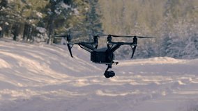 Slow motion of a black drone functioning in the sub zero temperatures, snow covered ground in the background, 23.98 fps.