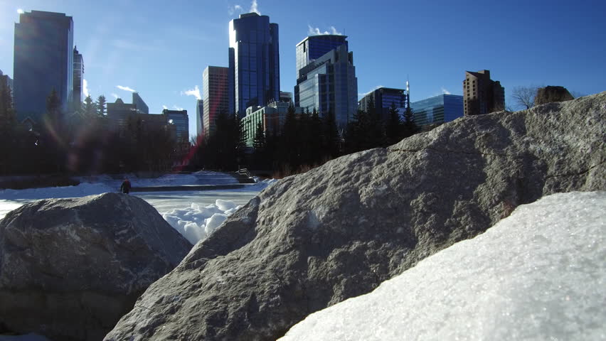 Jib move along frozen pond with skyline of the City of Calgary in behind.  People skating on the pond.
