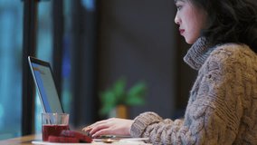 Side view of one pretty young Asian woman typing on laptop in the cafe by the window, female freelancer busy working on computer, urban lifestyle 4k clip.